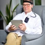 Man sitting in armchair using a neurofeedback device with tablet indoors.